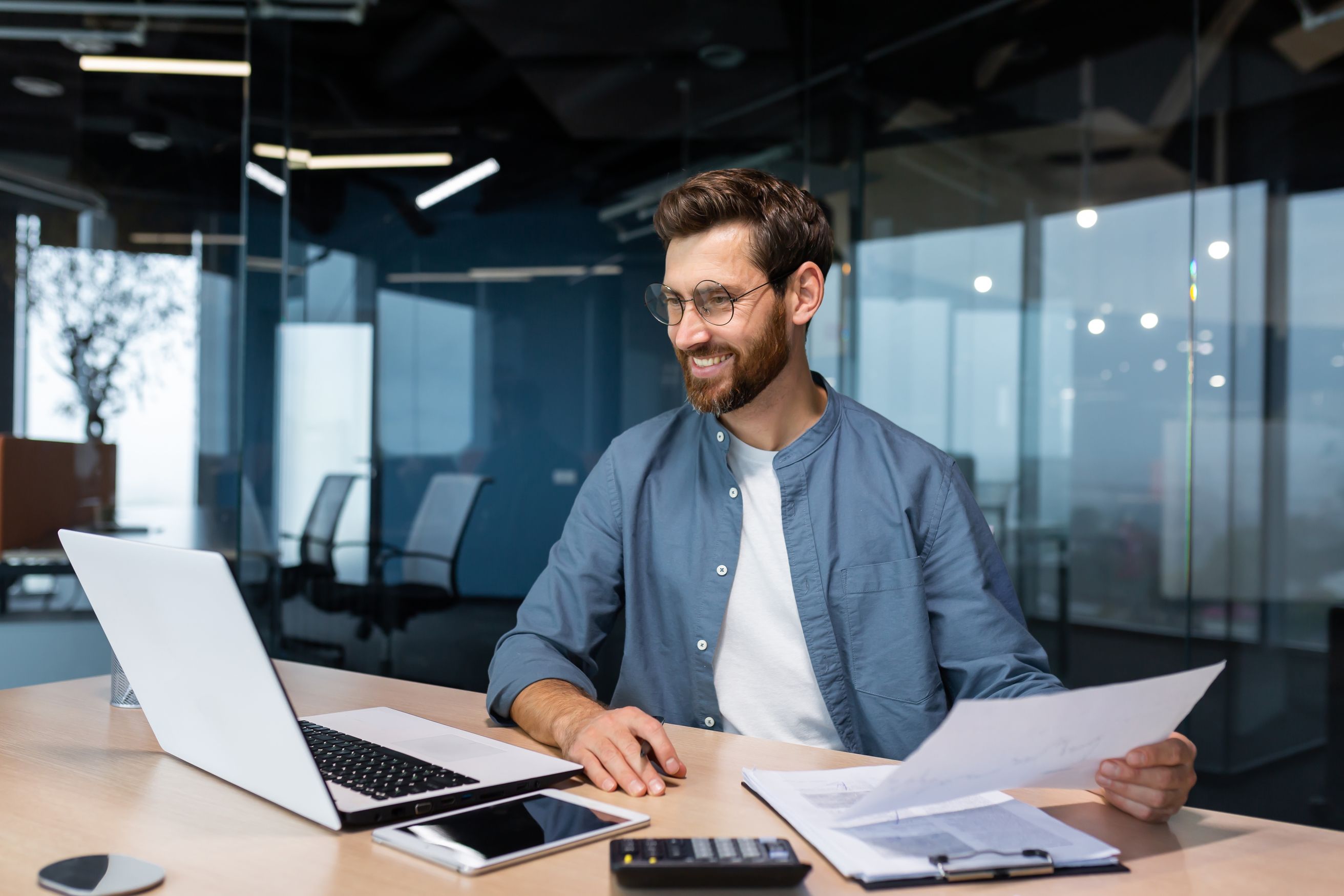 Employee looking at his laptop while holding printed data 