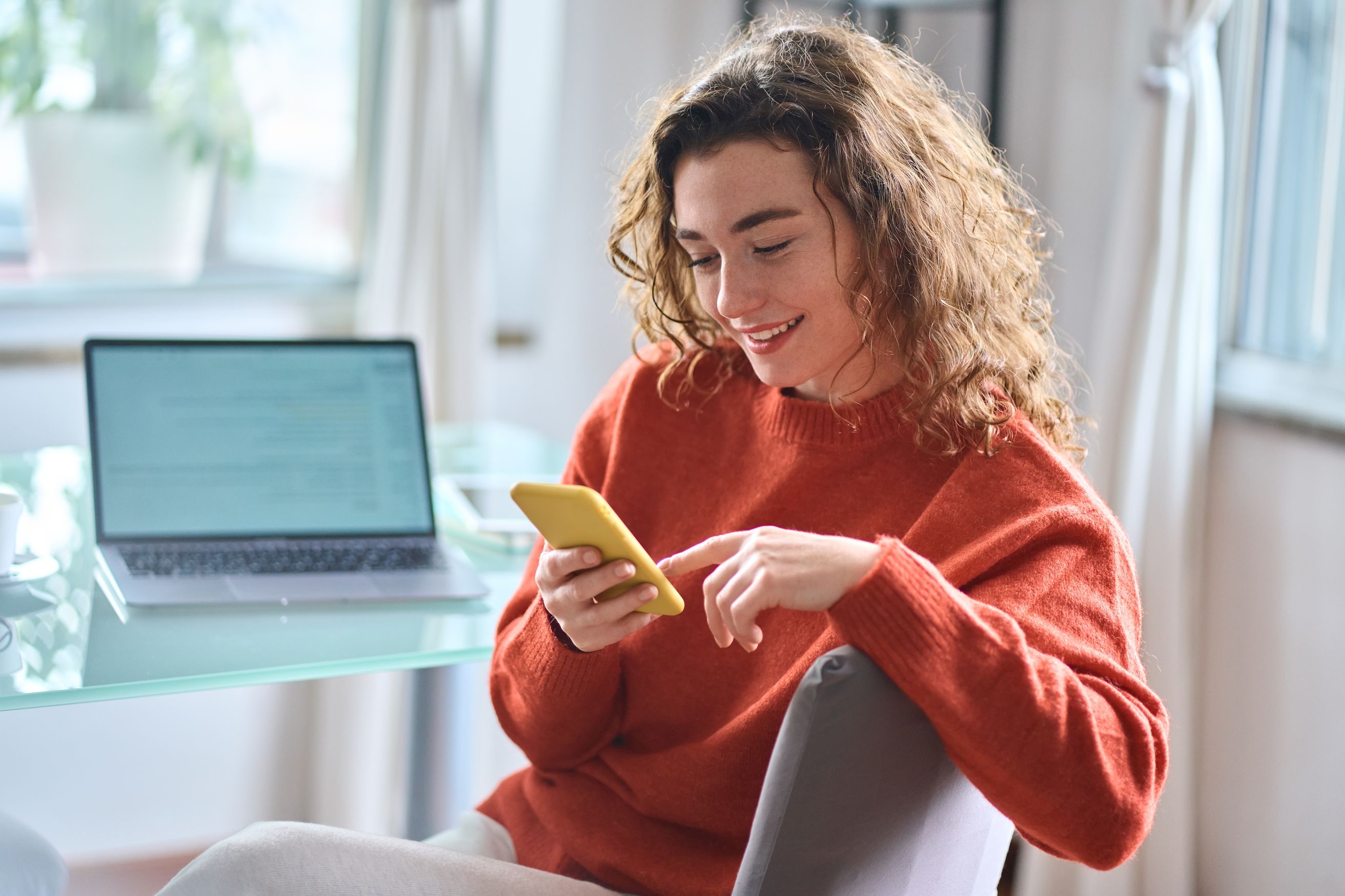 woman in red sweater touching her mobile phone while sitting at a desk