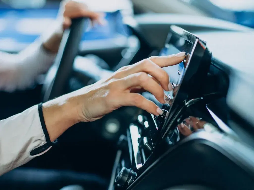 Person adjusting a touchscreen interface in a modern car dashboard.