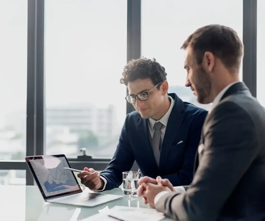 Two professionals review financial data on a laptop, discussing AI-driven insights in investment strategy.