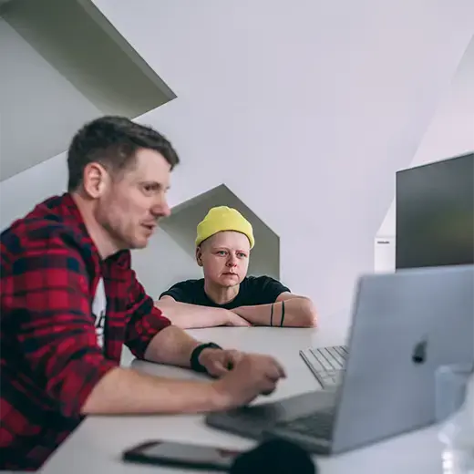 two coworkers sitting at a desk looking at computer monitors