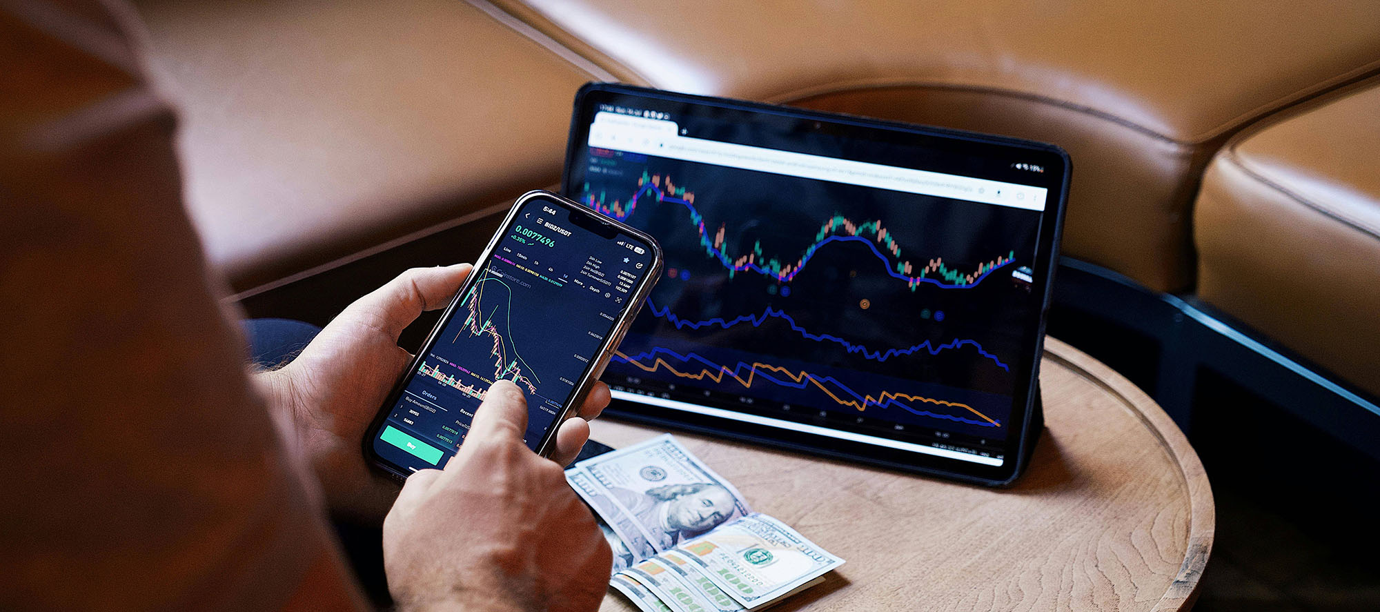 Person holding mobile phone with market data and a tablet on the table