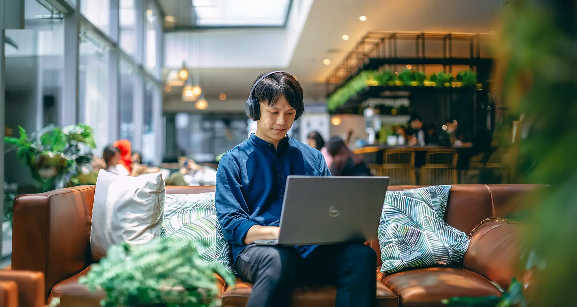 A man wearing a headphone is sitting on the sofa and doing work on his laptop