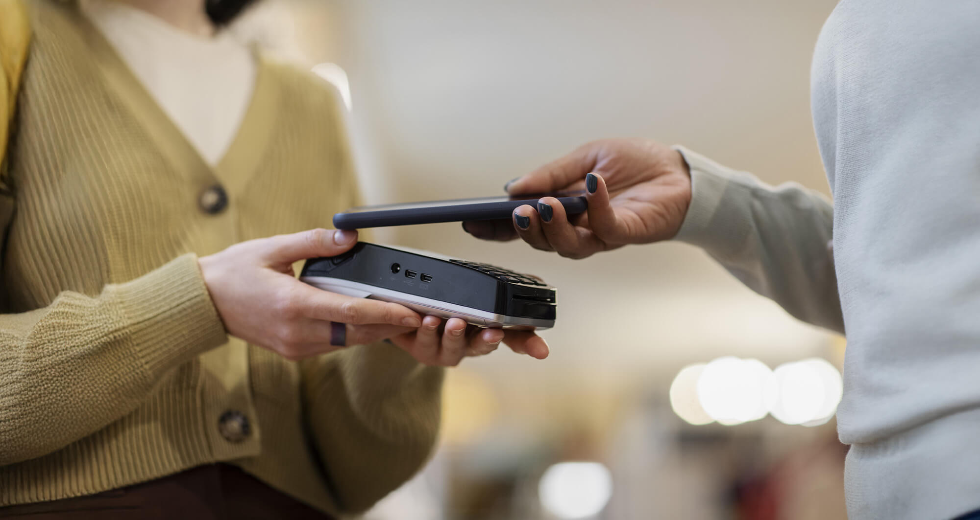 Customer making a contactless payment using a smartphone and card reader in a retail environment.