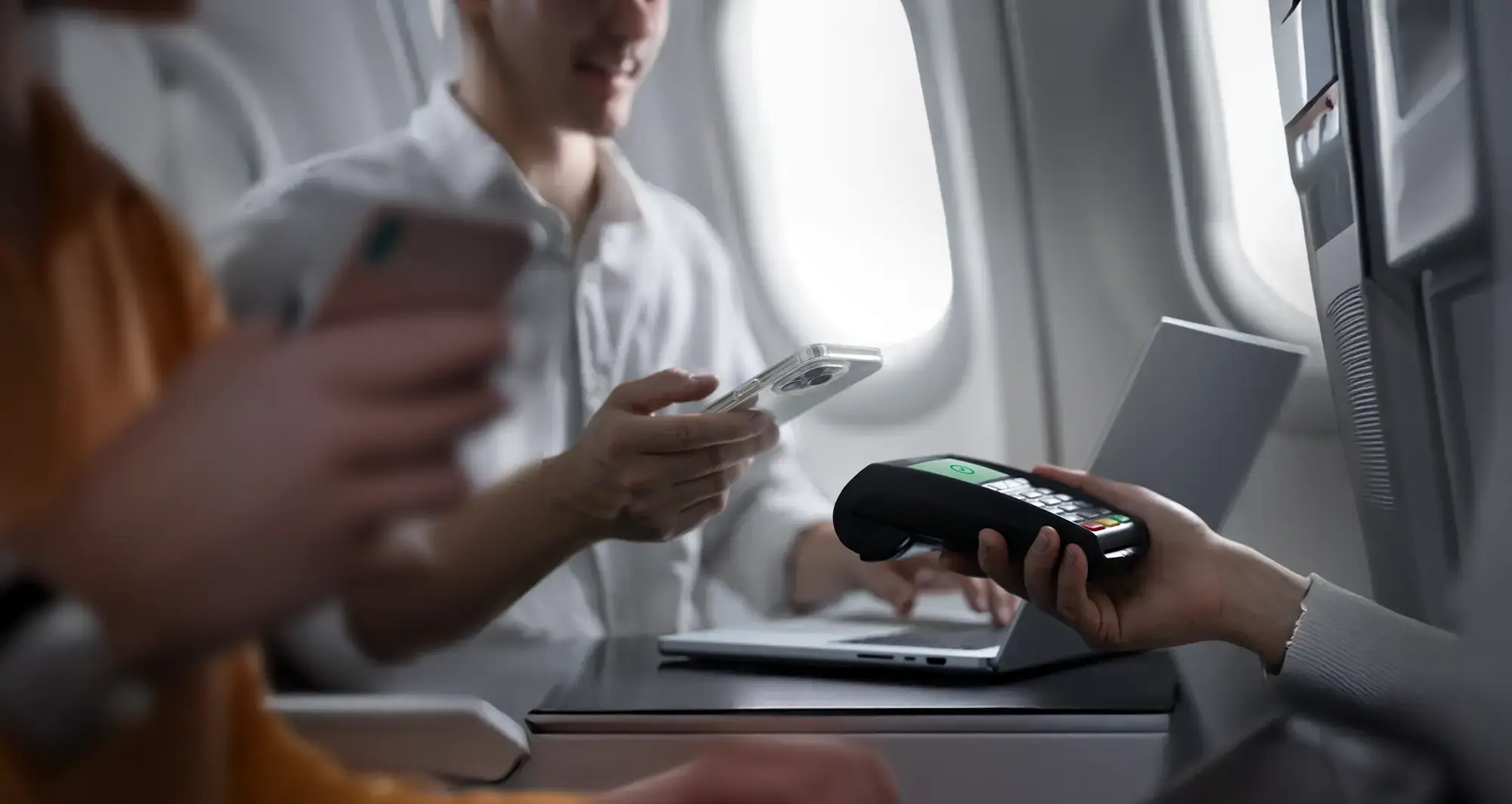 Passenger uses smartphone for contactless payment via card reader on airplane tray table.