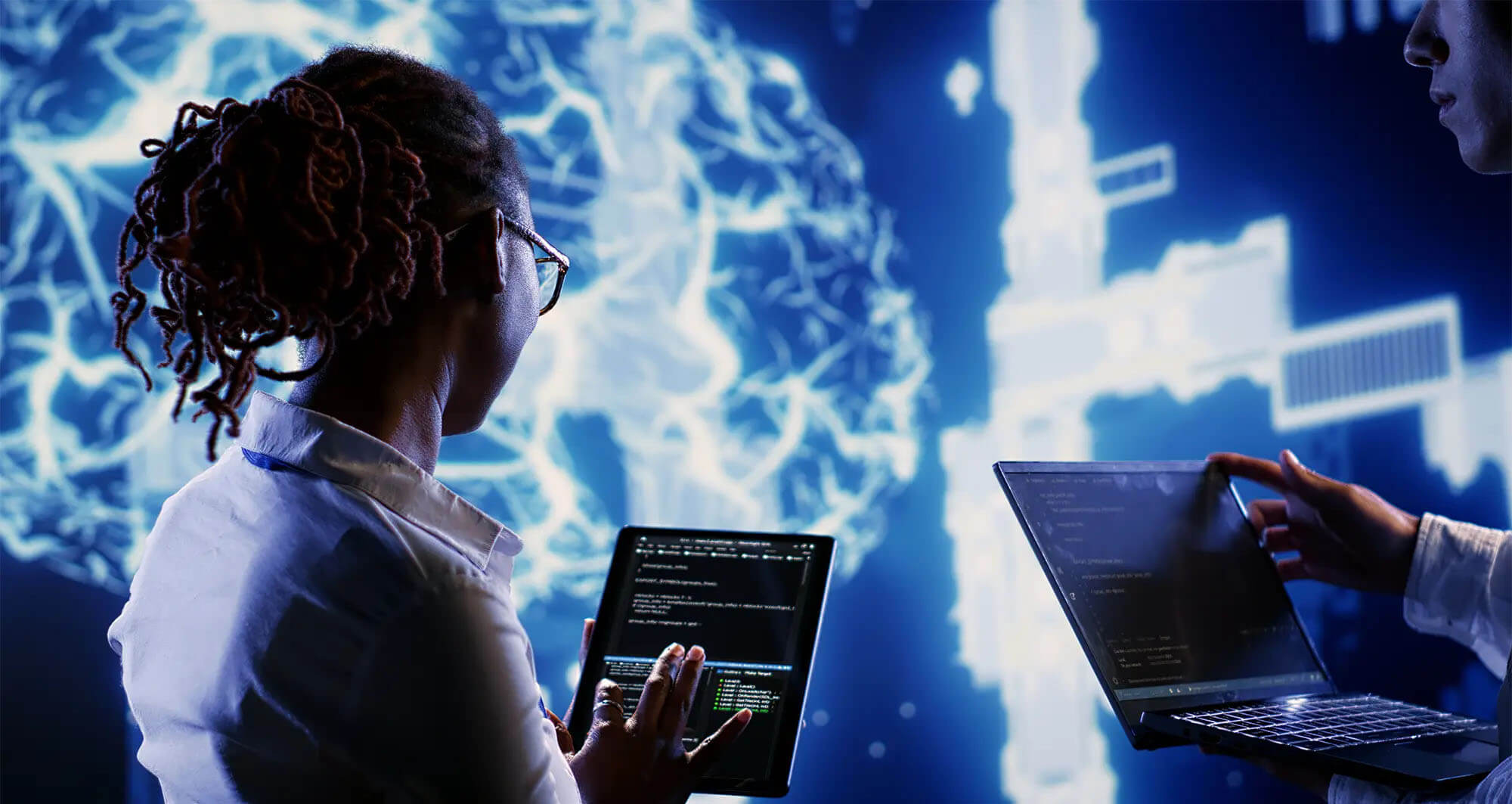 Developers coding with tablets and laptops in front of a glowing digital brain interface.
