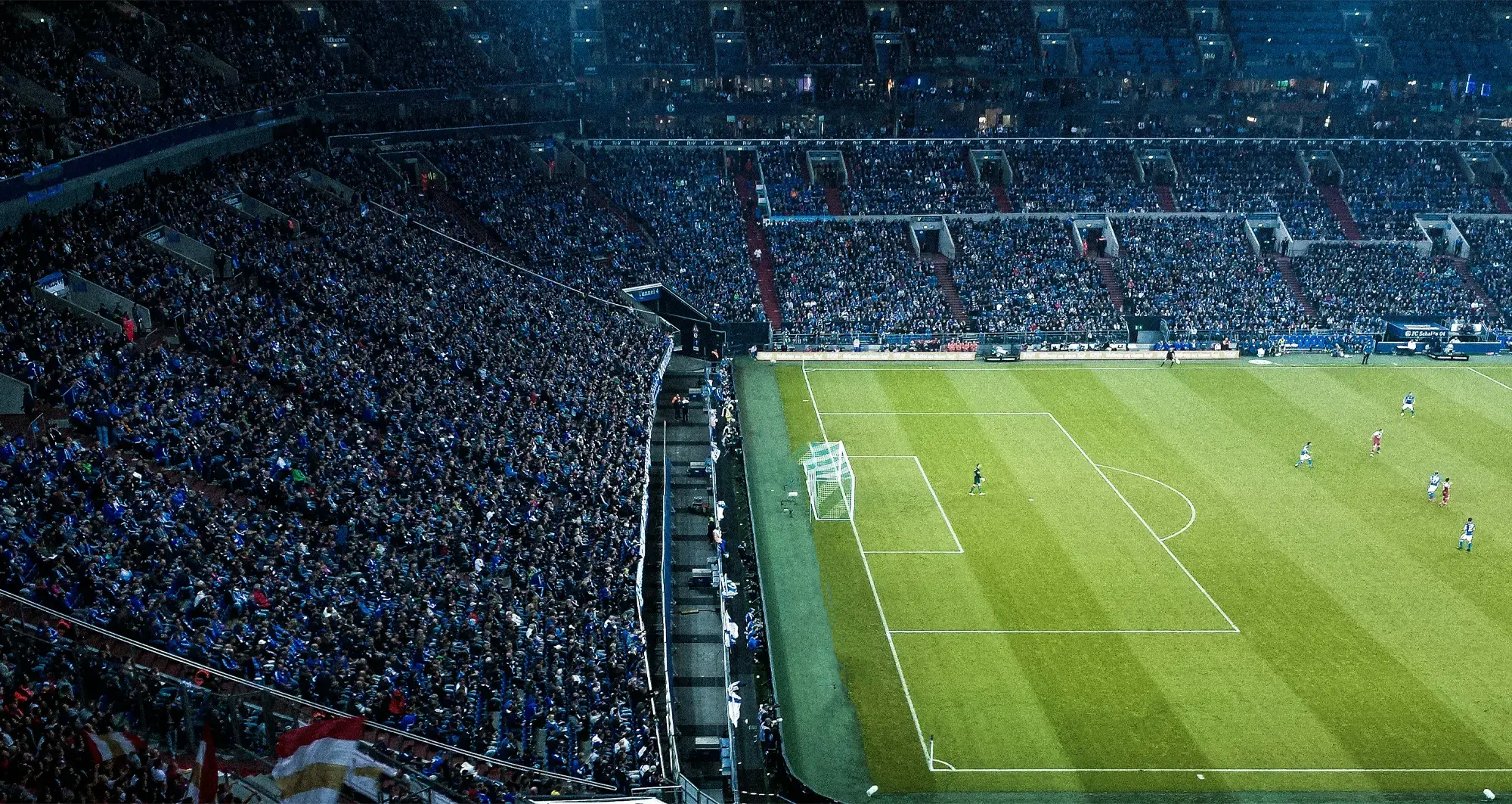 Packed football stadium with fans in the stands and a goalkeeper on the pitch near the goalpost during a match.