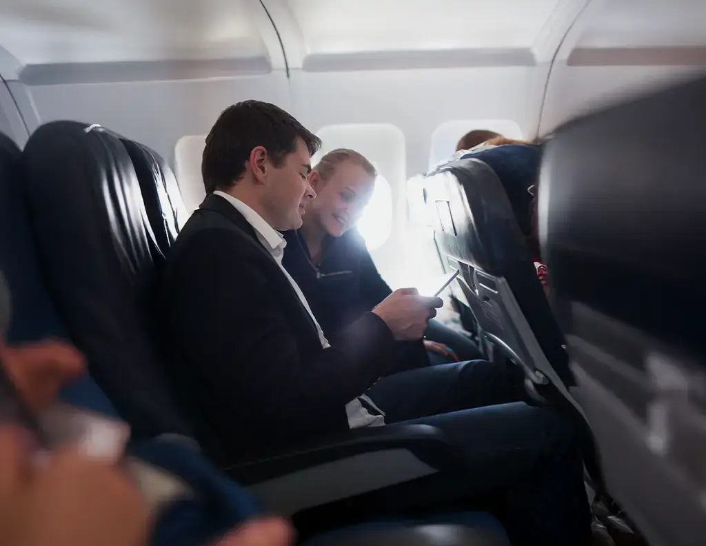 man and woman in airplane seats viewing app on phone