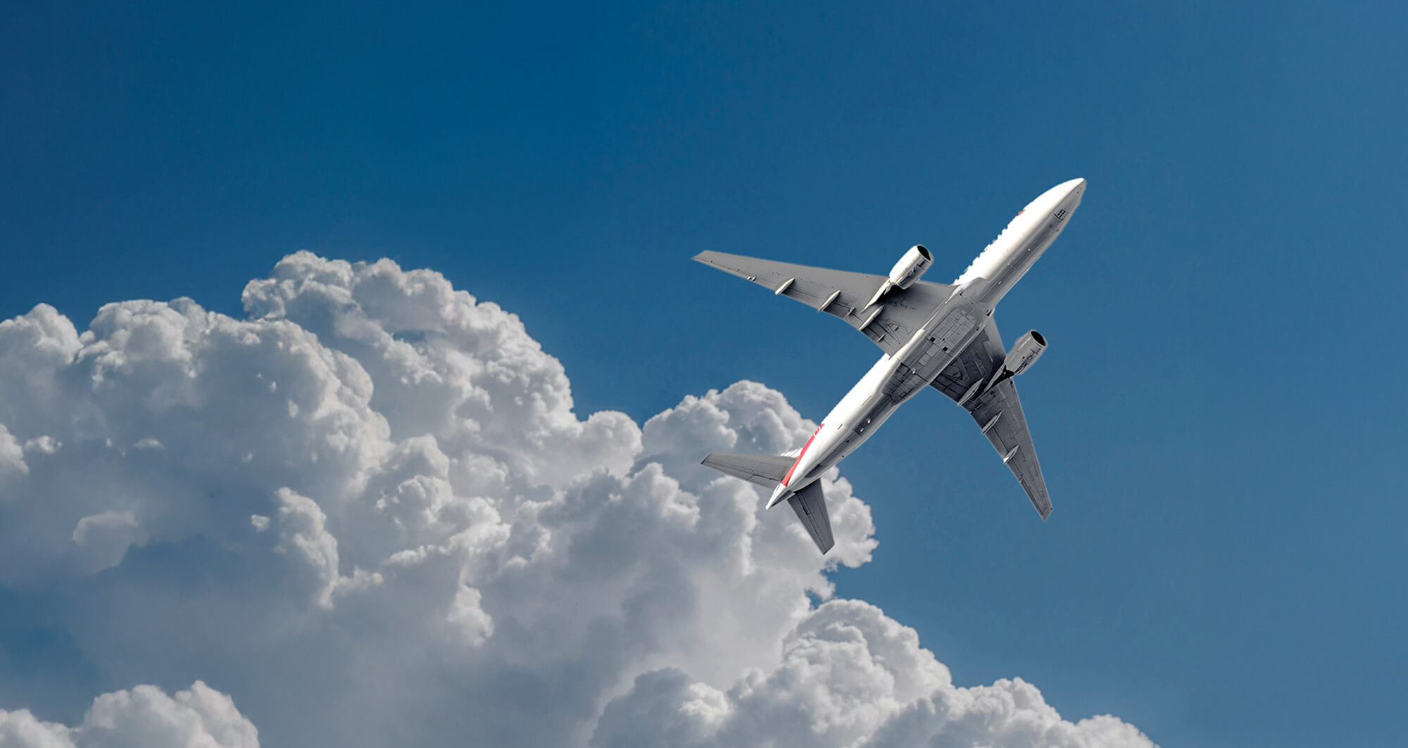 Airplane banking above dense clouds against a clear blue sky, representing dynamic air travel technology.
