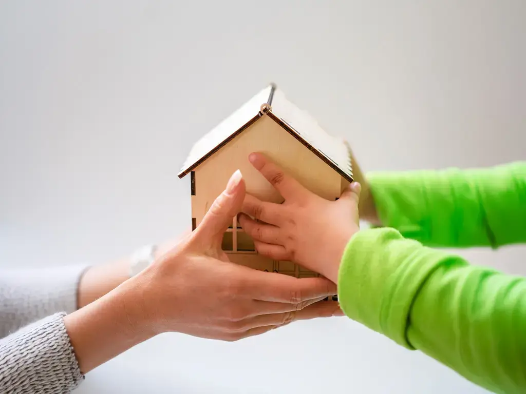 Hands holding a model home, representing claims intelligence for insurance leaders.