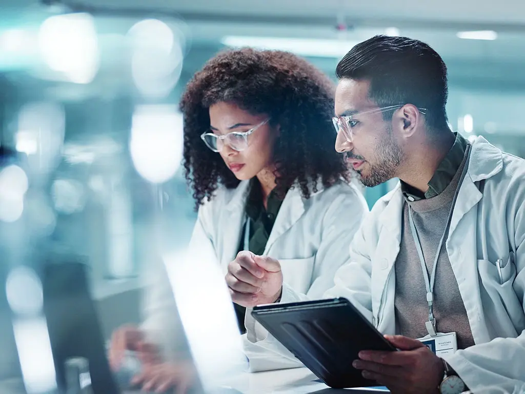 Researchers in lab coats analyzing data on a tablet and laptop in a modern laboratory.